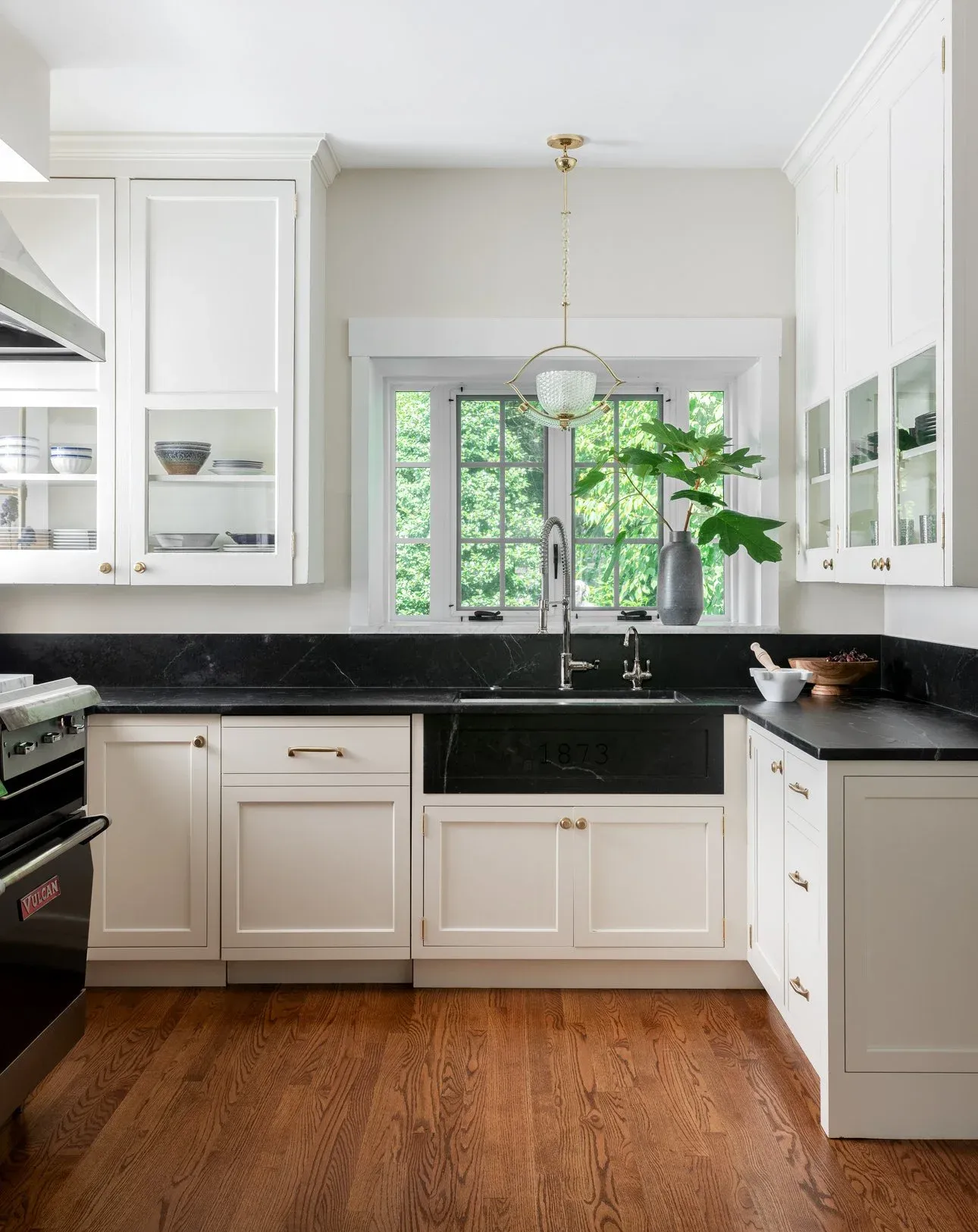 White kitchen with dark soapstone countertops and brass pendant light