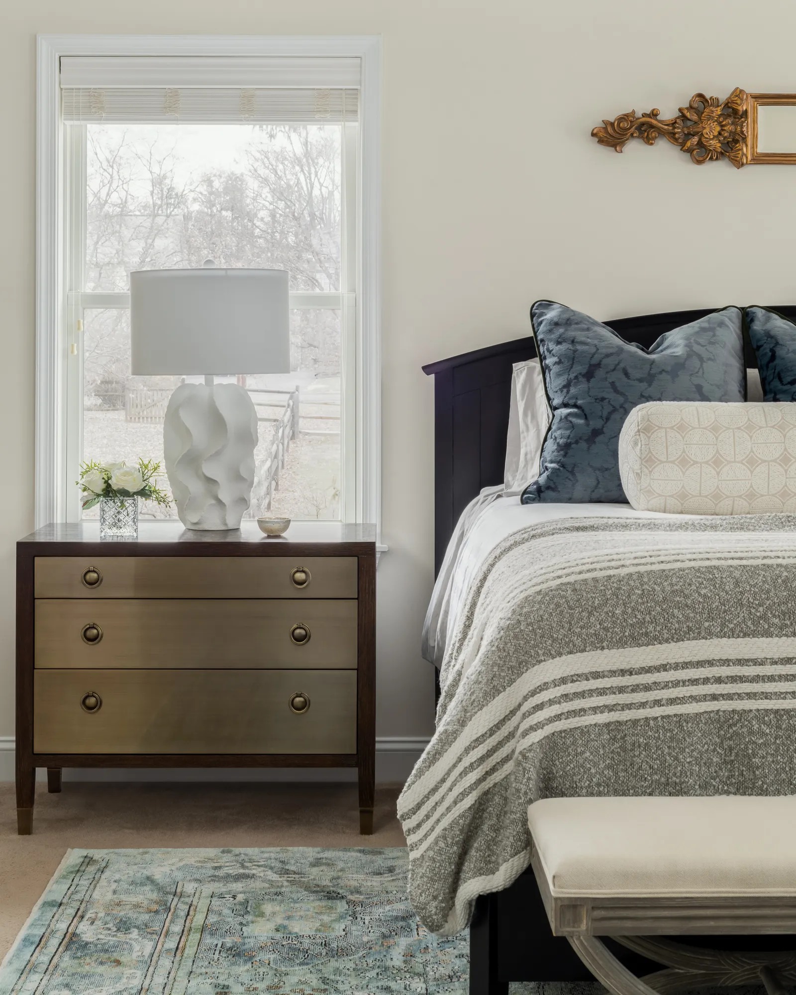 Bedroom with brass-front nightstand, sculptural white lamp, and blue accent pillows