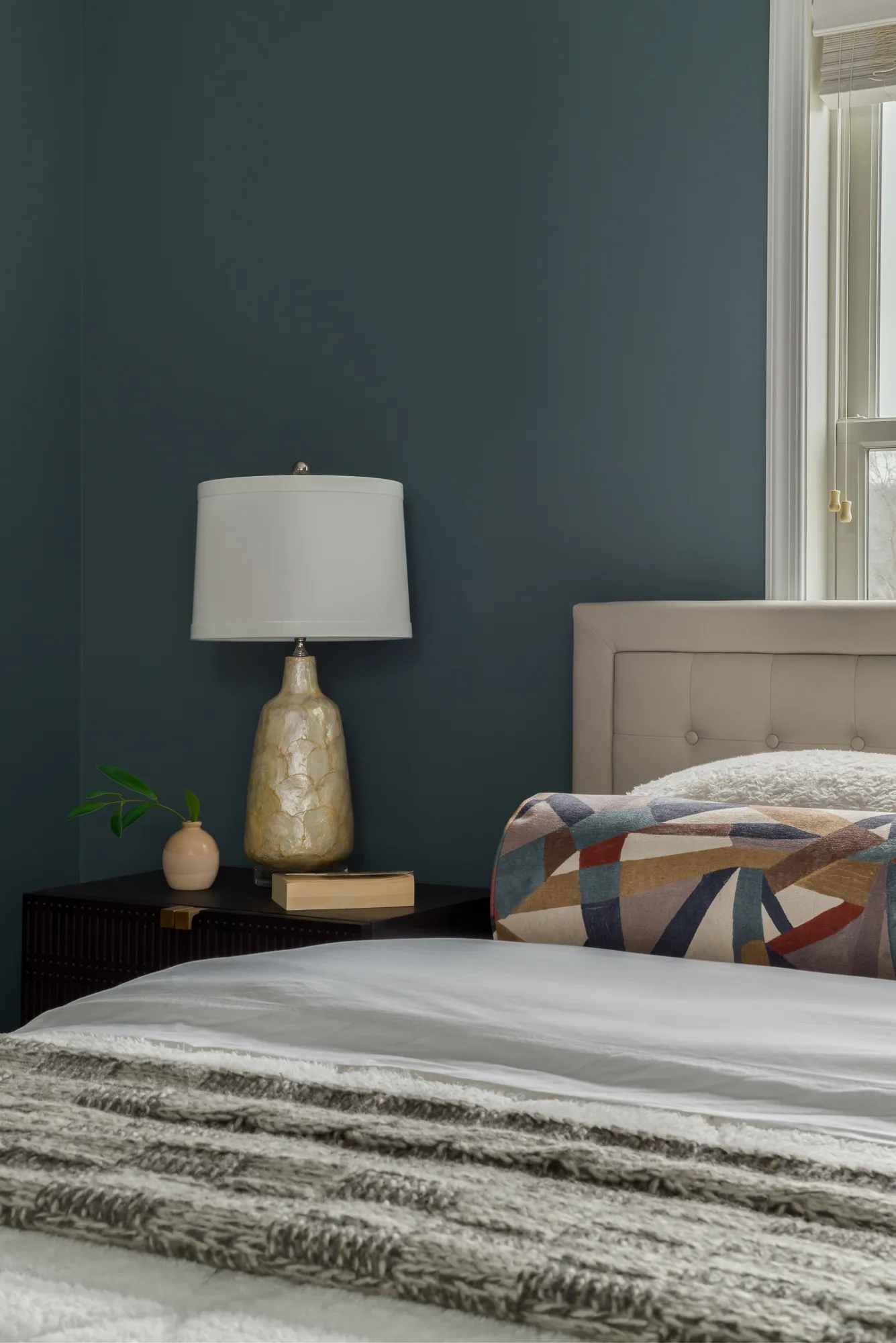 Teal guest room nightstand with brass sconce and stacked books