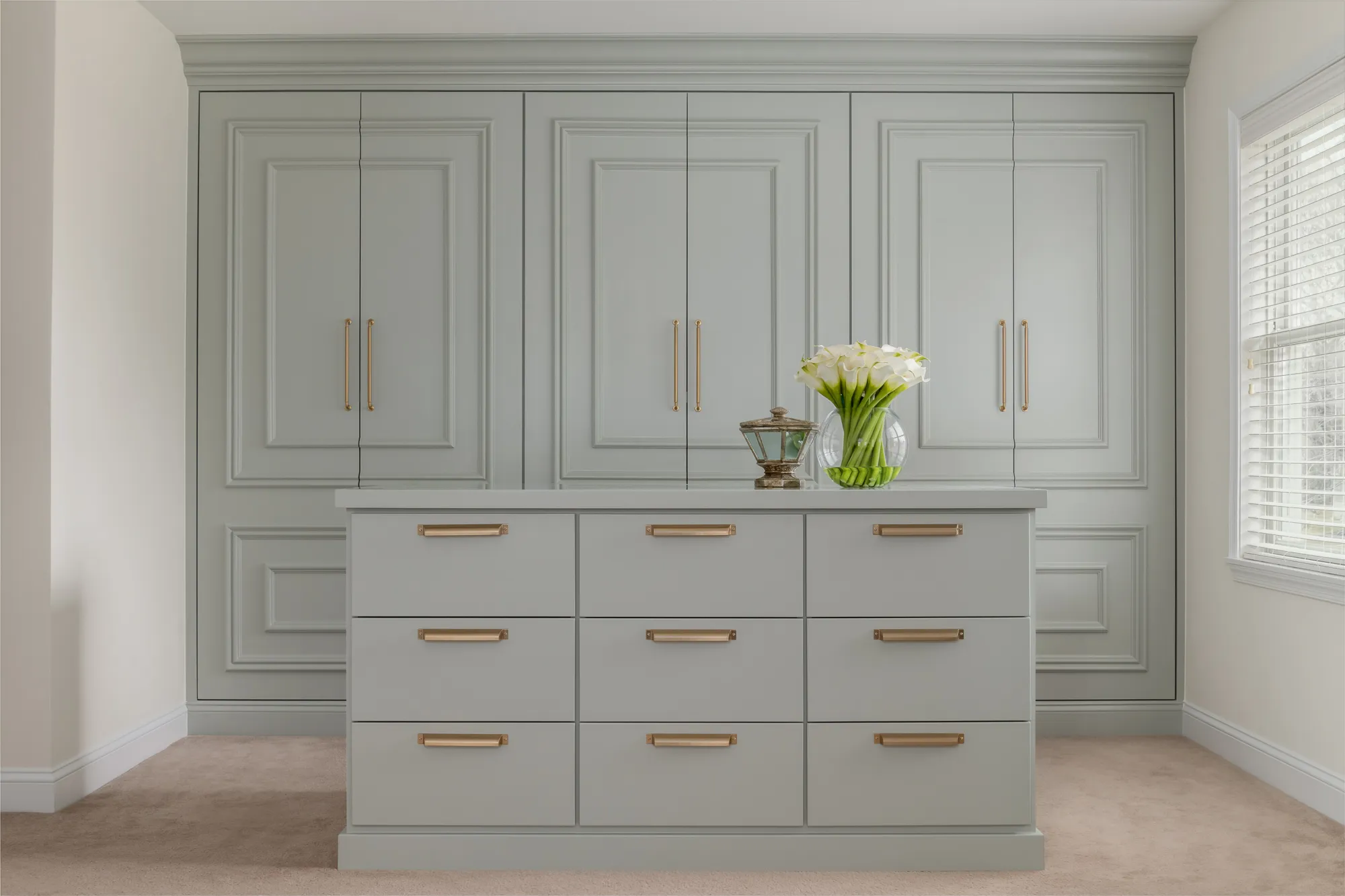Walk-in closet with pale sage cabinetry and brass hardware