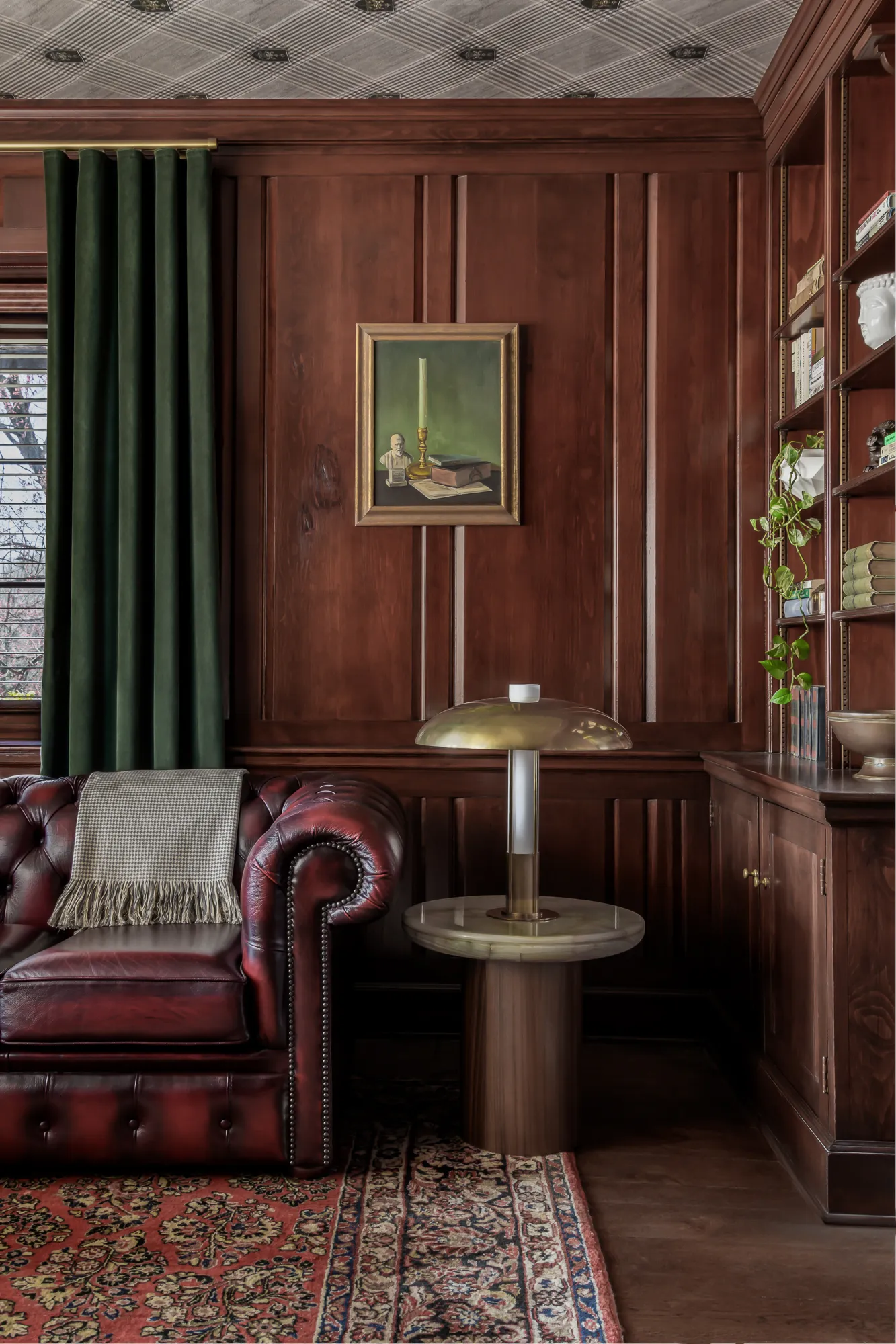 Chesterfield sofa corner with oil painting, brass mushroom lamp, and emerald drapes