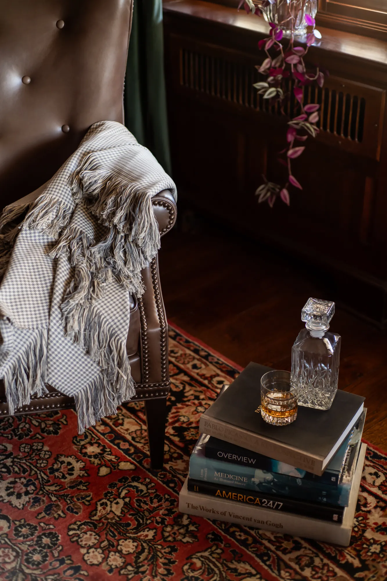 Library detail with houndstooth throw, crystal decanter, and stacked books
