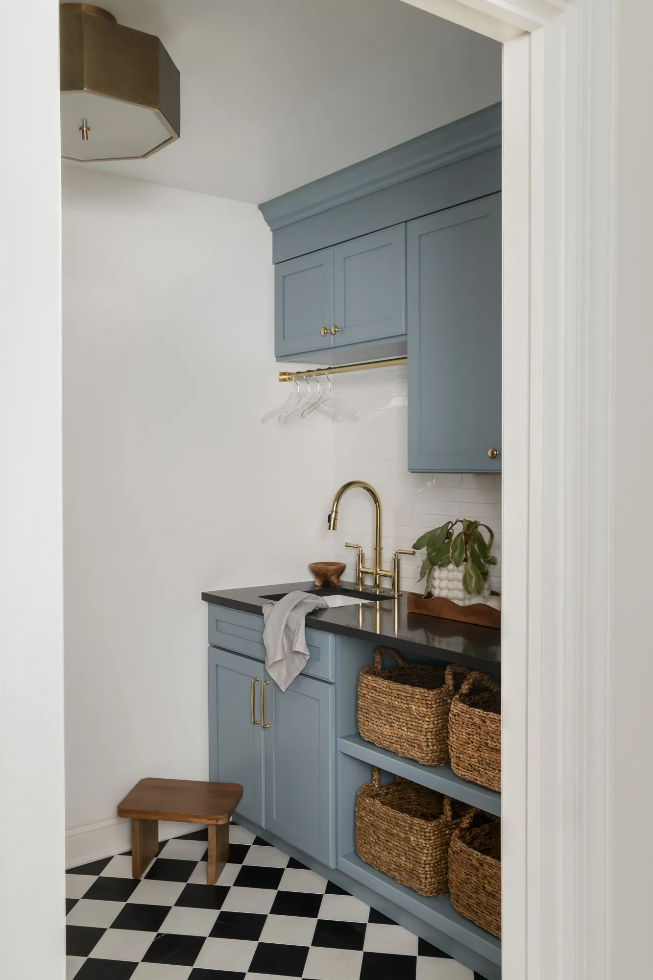 Laundry room with dusty blue cabinetry, checkered floor, and brass fixtures