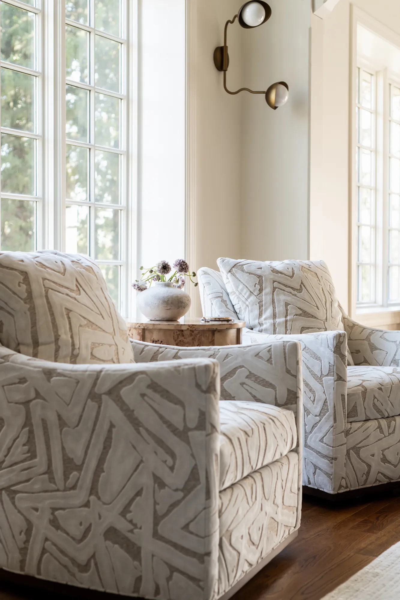 Patterned accent chairs with burled wood table and brass wavy sconce