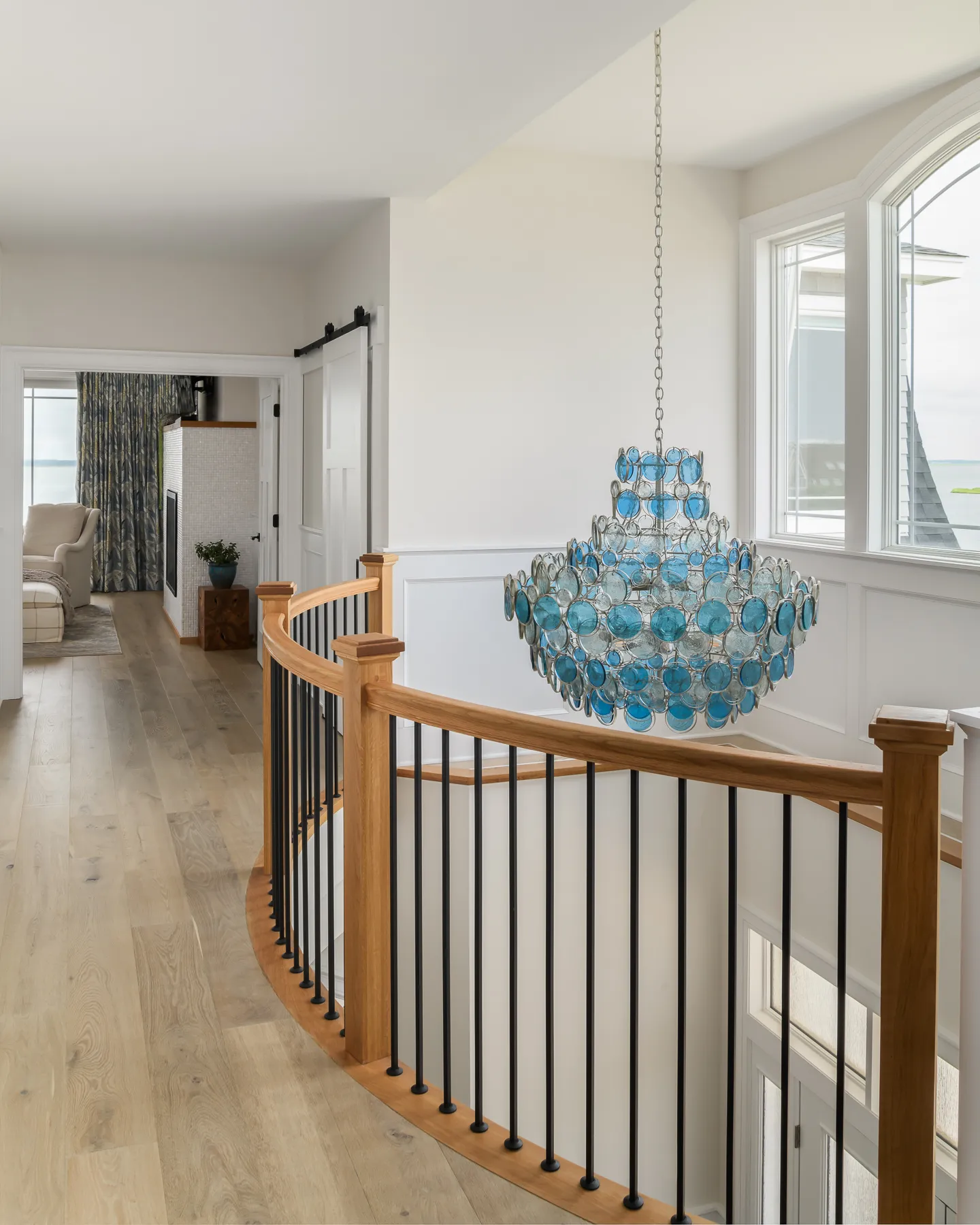 Curved upper landing with blue sea glass chandelier and barn door