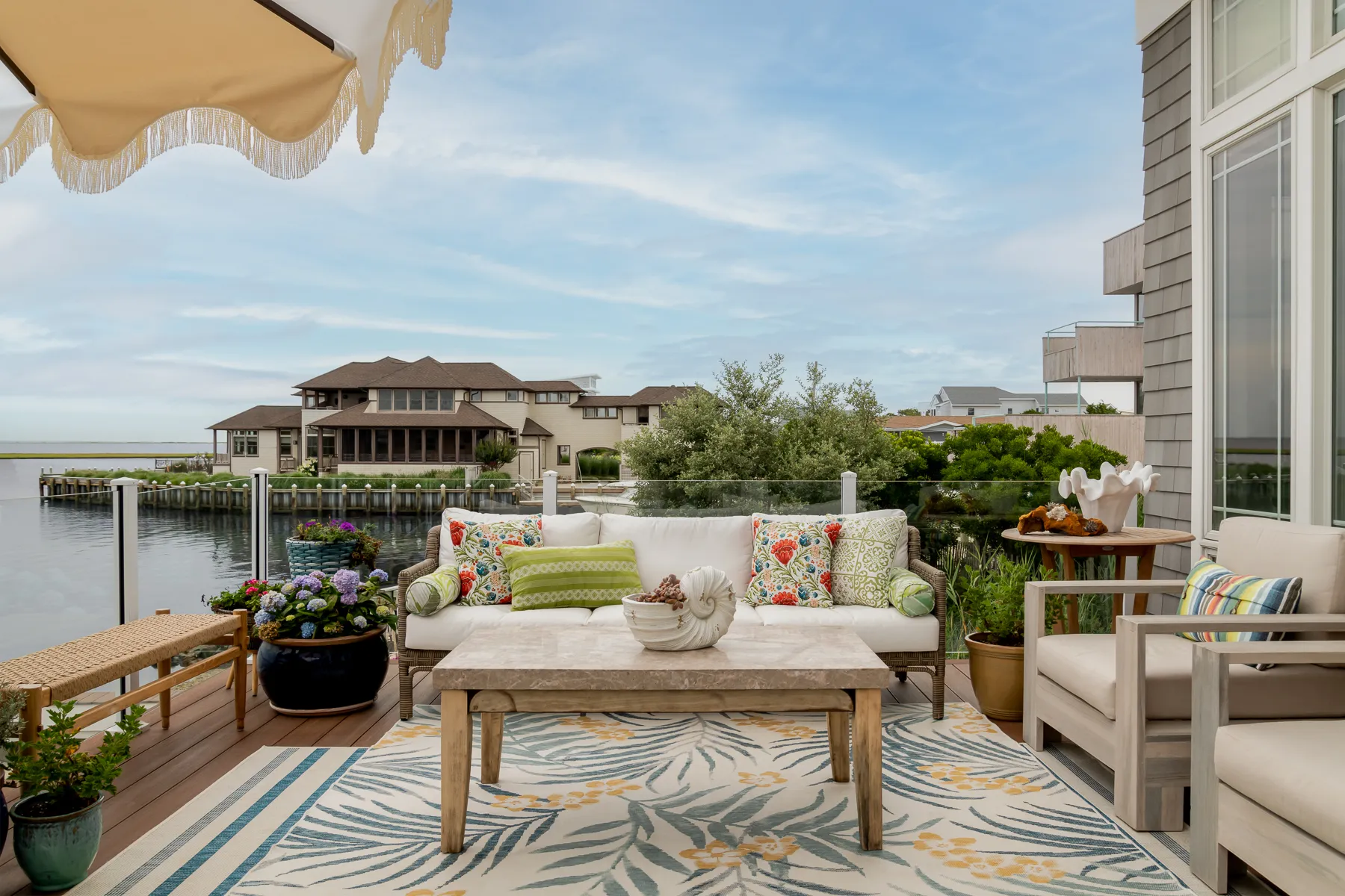 Bayside deck seating with colorful floral pillows, fringed umbrella, and waterfront views