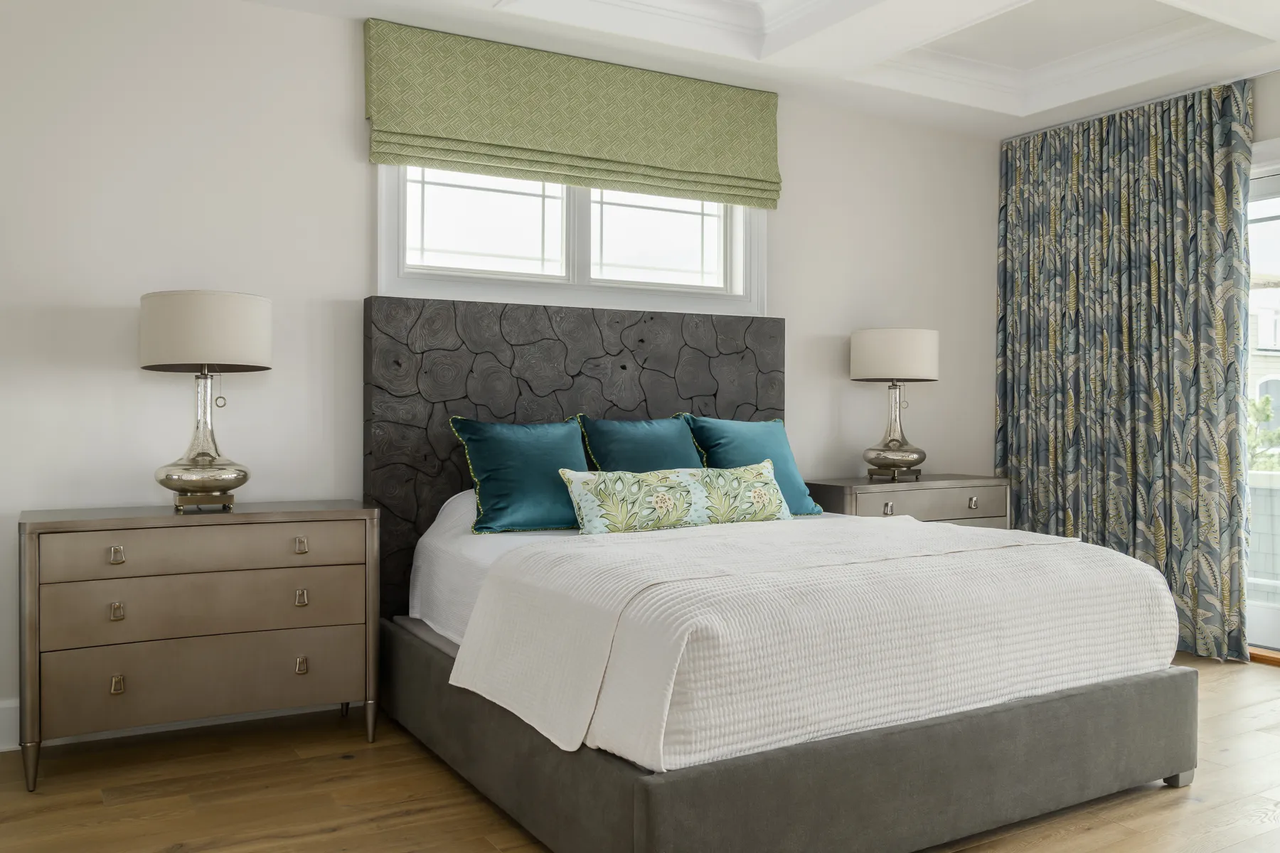Primary bedroom with sculptural charcoal headboard, teal velvet pillows, and botanical drapery