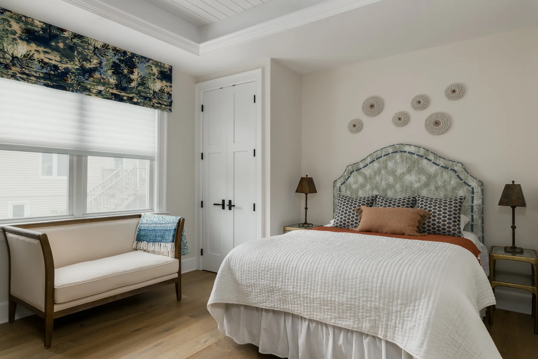 Guest bedroom with arched upholstered headboard, toile valance, and sea urchin wall art