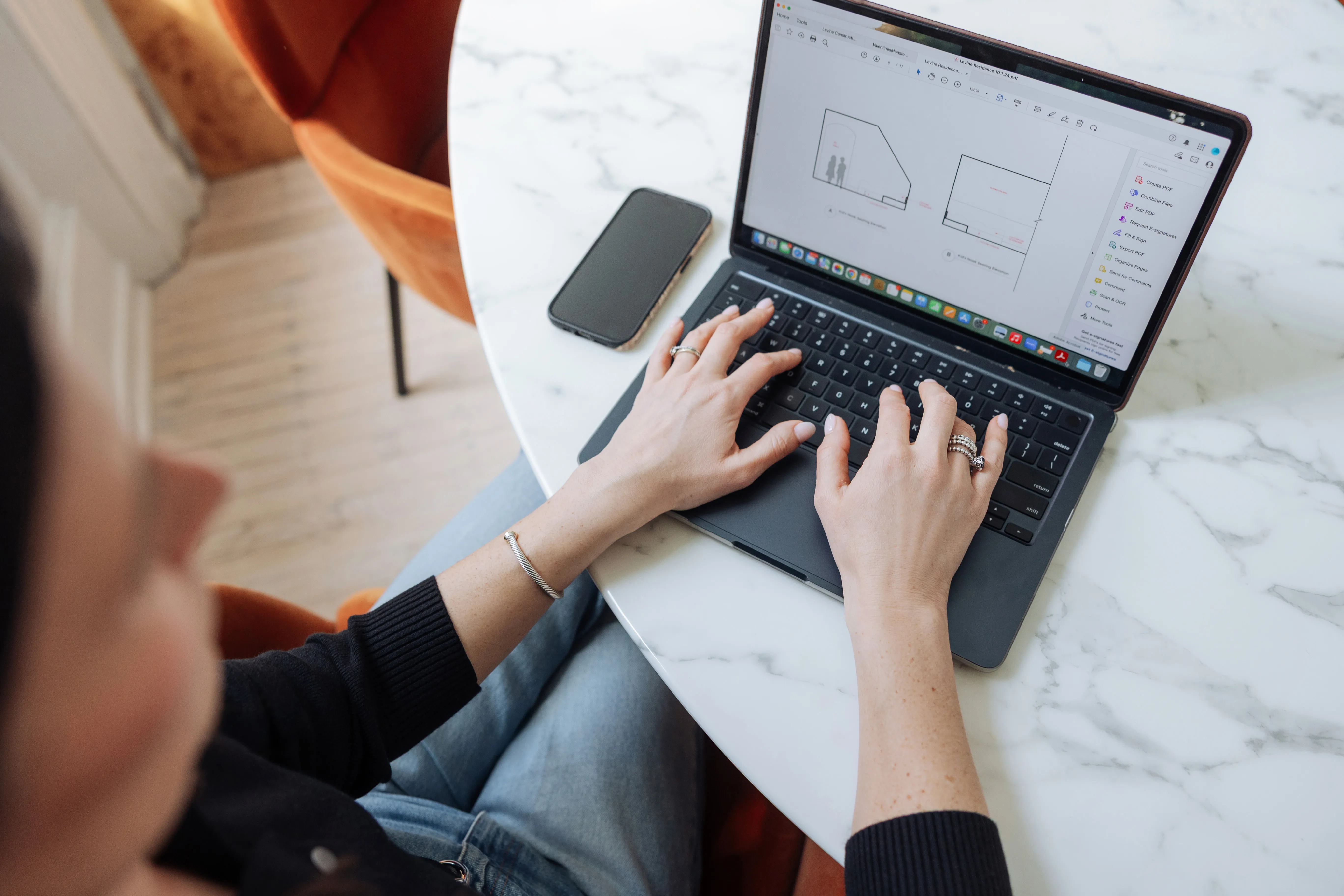 Designer coordinating project details on laptop with design plans on screen