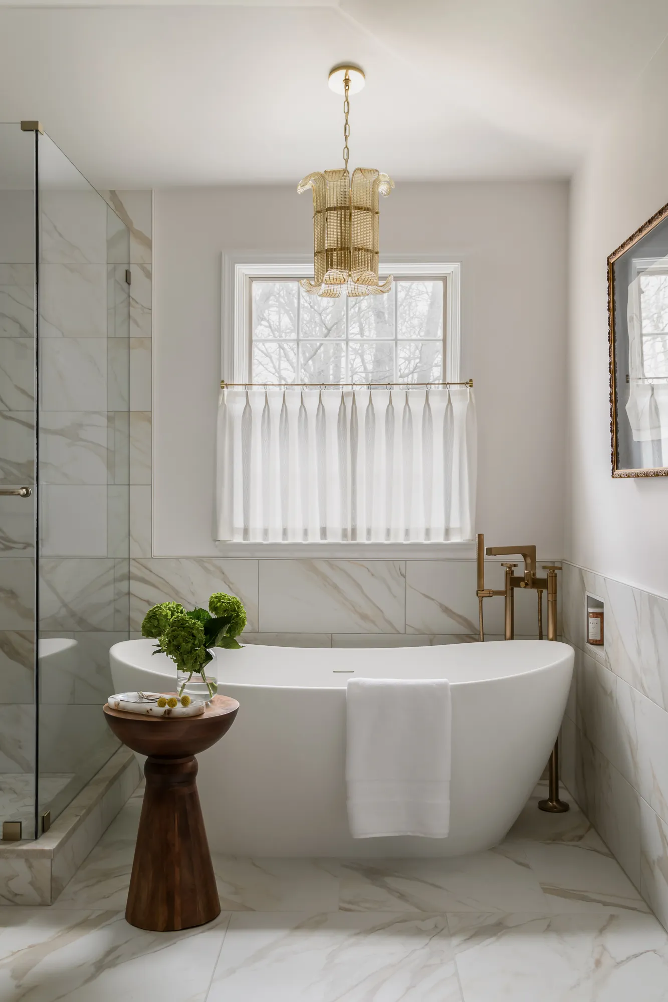 Freestanding tub with gold chain pendant, marble surround, and cafe curtain