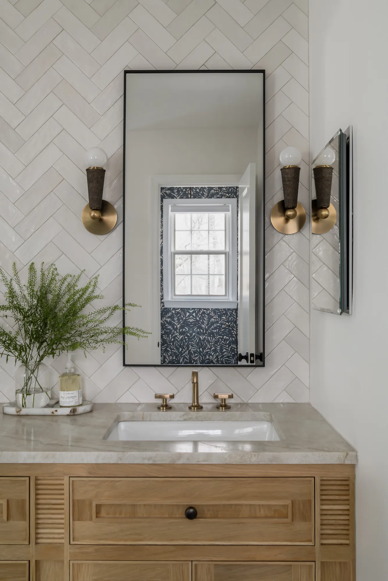 Single vanity sink with brass sconces and herringbone tile